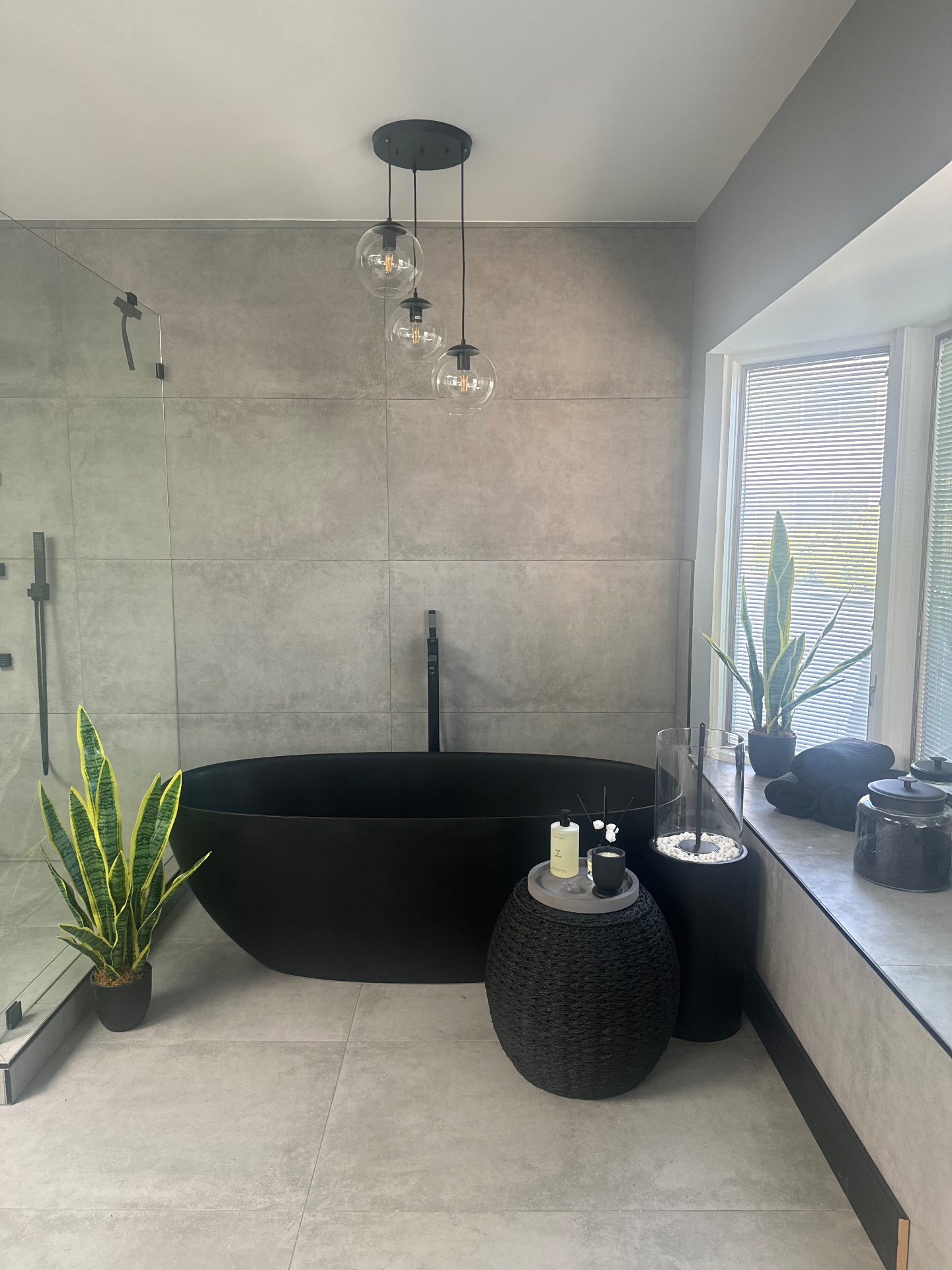 Freestanding matte black soaking tub with concrete tile walls and pendant lighting