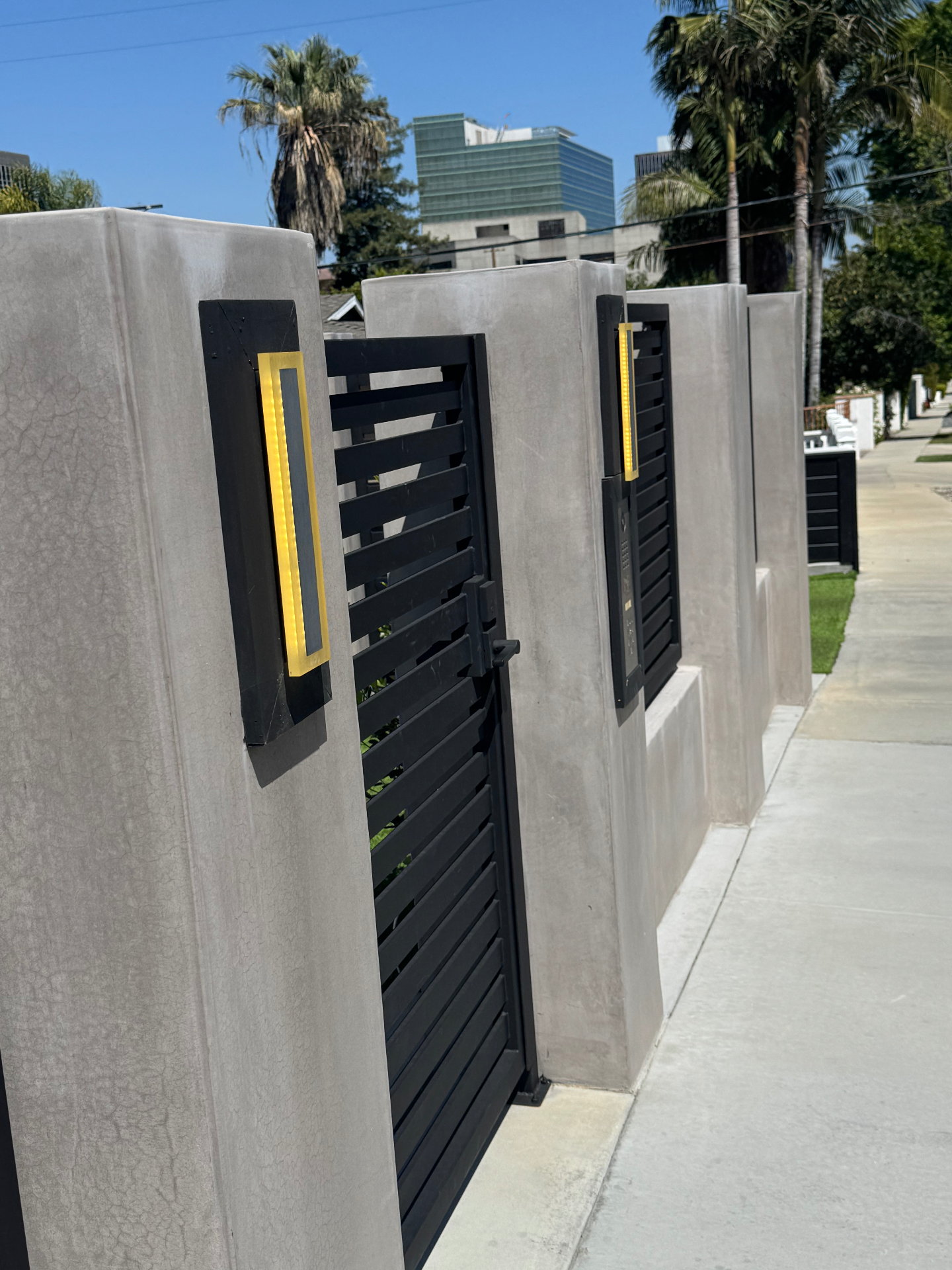 Black horizontal slat pedestrian gate with concrete columns, LED sconces, and video intercom