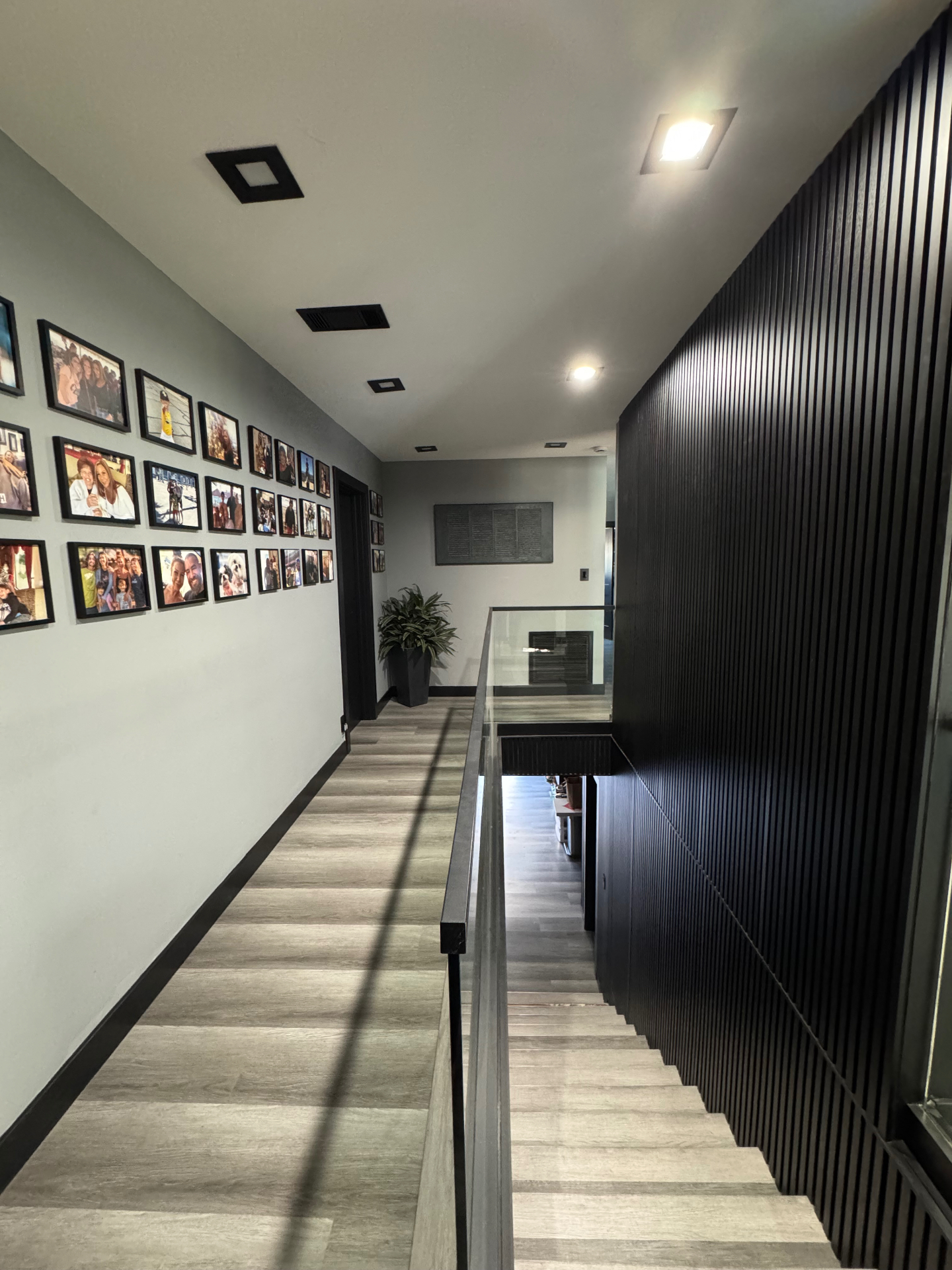 Staircase remodel with frameless glass railing, black slat wall, and family photo gallery