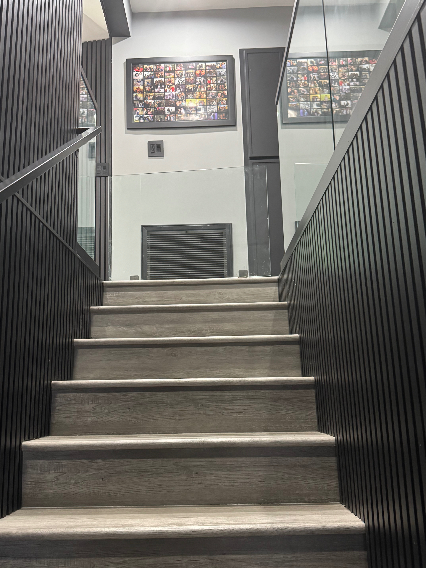 Modern staircase with wood-look treads, black slat walls, and glass railing